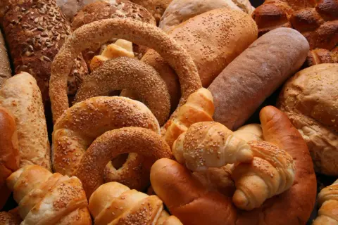 Różnorodne rodzaje chleba i bułek, w tym bochenki z ziarnami, precle z sezamem i rogaliki, tworzą apetyczną kompozycję.