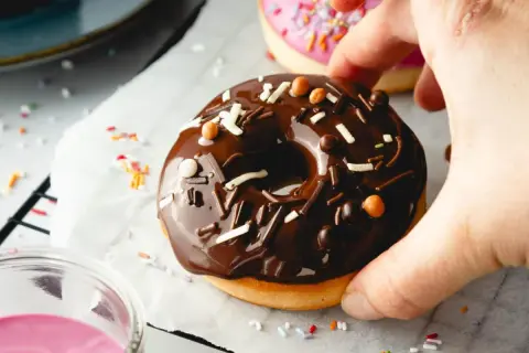 Leckeres Schoko-Donut-Rezept für den Backofen. Ein Donut mit Schokoglasur und Streuseln wird von einer Hand gehalten.