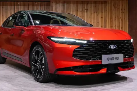 Nowy, lśniący, czerwony Ford Mondeo MK5 z czarnym dachem i felgami prezentuje się elegancko na tle drewnianej ściany.
