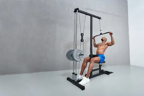 Man tränar latsdrag muskler på ett gym. Han sitter på en bänk och drar ner en stång med vikter.