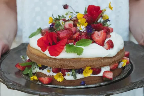 En vacker sommartårta med jordgubbar, grädde och vilda blommor på ett silverfat. Perfekt för en solig dag.