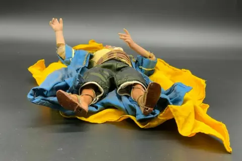 Eine Krippenfigur des heiligen Josef liegt erschöpft auf einem blauen und gelben Tuch.