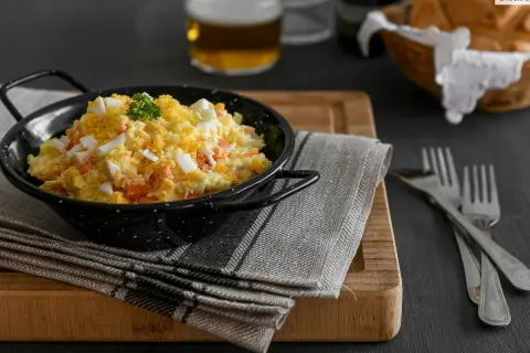 Una deliciosa ensalada rusa, cremosa y con trozos de huevo duro y zanahoria, servida en un cuenco negro.