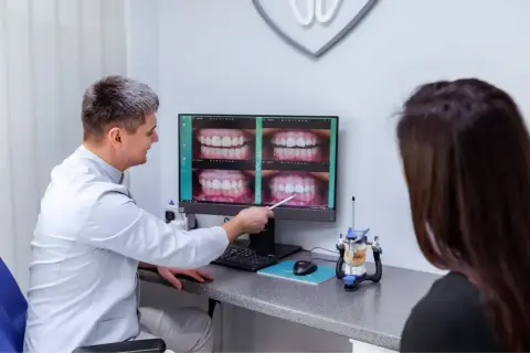 Stomatolog pokazuje pacjentce zdjęcia uśmiechów na monitorze.