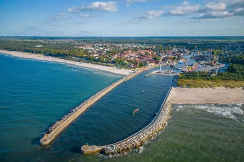 Widok z lotu ptaka na port w Ustce z falochronami, plażą i miastem w tle.