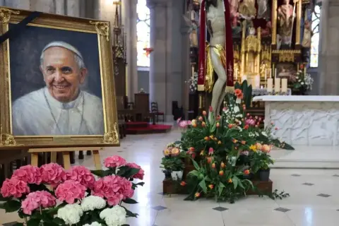 Obraz ojca świętego Franciszka w kościele, otoczony kwiatami i krzyżem.