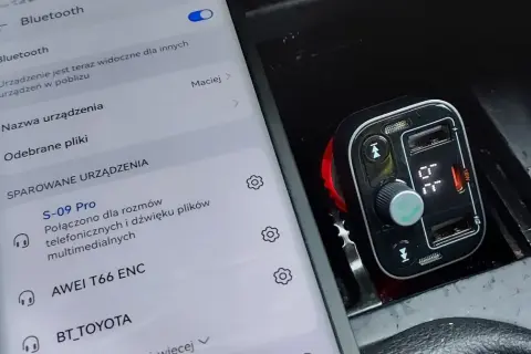 Jak ustawić transmiter w aucie? Na ekranie telefonu widać menu Bluetooth, a obok transmiter samochodowy podłączony do gniazda zapalniczki.