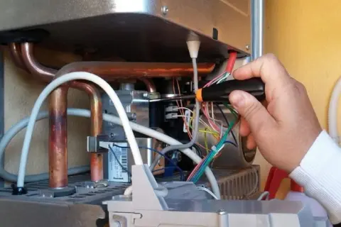 Tecnico effettua la pulizia della caldaia, lavorando sui cablaggi interni con un cacciavite.