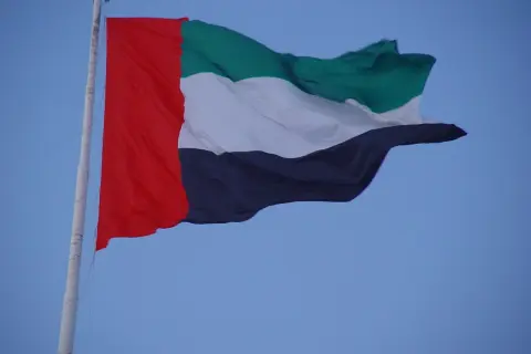 Flaga Zjednoczonych Emiratów Arabskich powiewa na maszcie na tle błękitnego nieba.