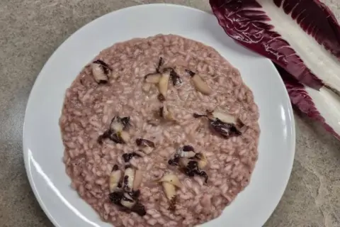 Un cremoso risotto al radicchio, con pezzetti di verdura che spuntano, accanto a una foglia fresca di radicchio.