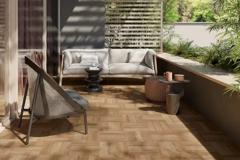 Terrazzo con pavimenti in gres porcellanato effetto legno, arredato con divano, poltrona e tavolini, immerso nel verde.