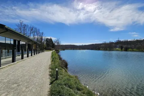 Promenade paisible au bord du lac de Flourens, avec un bâtiment moderne et un ciel bleu éclatant.