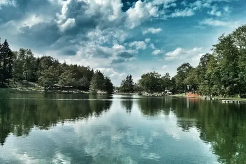 Un lago tranquillo circondato da alberi verdi, con nuvole drammatiche nel cielo. Un'oasi di pace tra i laghi dell'Emilia Romagna.