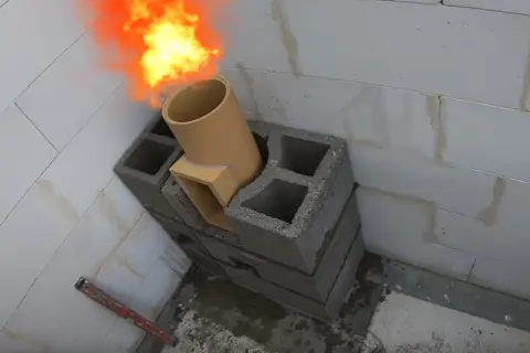 Rozpoczyna się murowanie komina systemowego. Płomienie wydobywają się z ceramicznej rury.