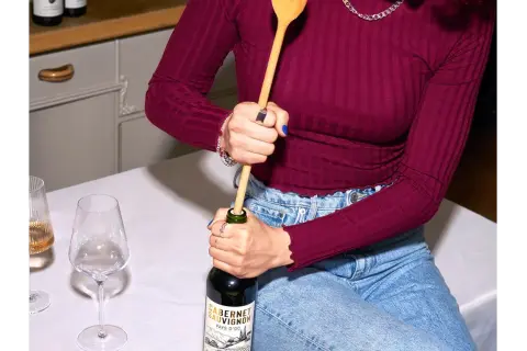 Korken ohne Korkenzieher: Eine Person versucht, eine Weinflasche mit einem Holzlöffel zu öffnen.