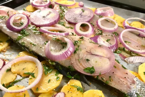 Lavarello in padella pronto per la cottura, con patate affettate, cipolla rossa a rondelle e prezzemolo fresco.