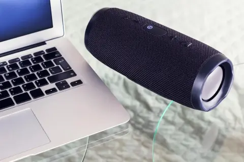 Un ordinateur portable et une enceinte Bluetooth noire sur une table en verre. Apprenez comment connecter une enceinte Bluetooth pour une expérience audio sans fil.