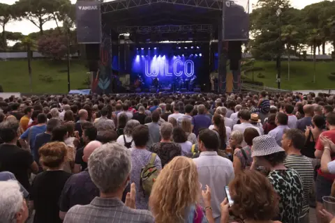 Gran concierto de Wilco en el **jardín de invierno Zaragoza**. Multitud disfruta al aire libre bajo un cielo crepuscular.