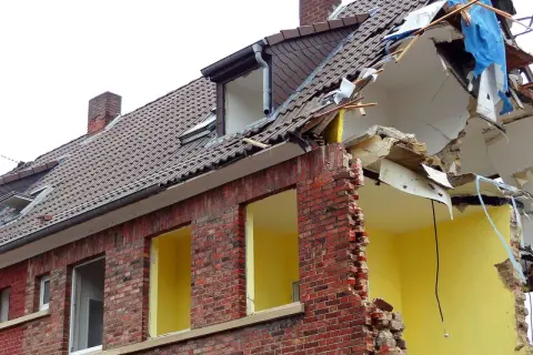 Zniszczony budynek z cegły, dach w trakcie rozbiórki. Jeśli planujesz wyburzenie budynku, sprawdź, gdzie zgłosić wyburzenie budynku.