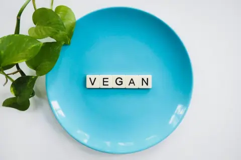 Niebieski talerz z literami "VEGAN" i zielonymi liśćmi. To symbol tego, co to jest weganizm – dieta bez produktów odzwierzęcych.