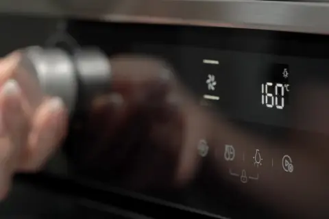 Dłoń obraca pokrętło piekarnika Whirlpool, wybierając funkcje oznaczone symbolami. Na wyświetlaczu 160°C.