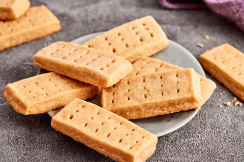 Goldbraune Shortbread-Kekse, perfekt für ein einfaches Shortbread Rezept. Sie liegen auf einem Teller und daneben ein lila Tuch.