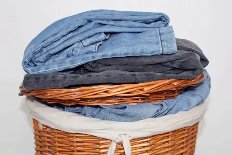 Ein Wäschekorb voller Jeans. Die oberste Jeans stinkt nach Chemie, ein deutliches Zeichen für eine neue Wäsche.