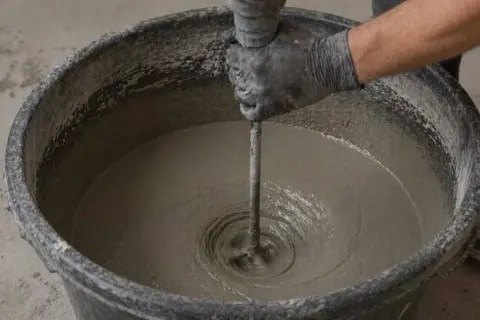 Mano guantata mescola cemento in un secchio, un passo fondamentale per imparare come fare stampi per cemento.