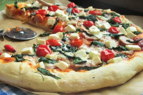 Pyszna pizza ze szpinakiem, pomidorkami koktajlowymi i kostkami sera feta. Idealna na szybki obiad.