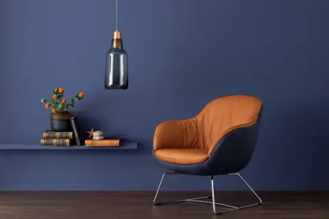 Ein Sessel mit cognacfarbenem Leder und dunkelblauem Stoff vor einer tiefblauen Wand. Die blau wandfarbe wirkung schafft eine ruhige Atmosphäre.