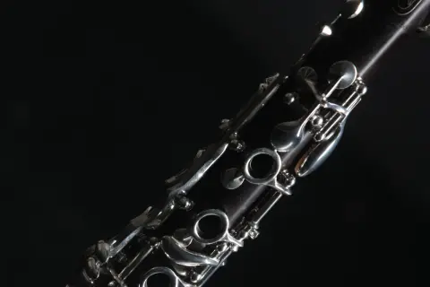 Nahaufnahme eines dunklen Holzblasinstruments, einer Klarinette, mit glänzenden Metallklappen vor schwarzem Hintergrund.