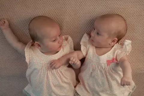 Två små bebisar ligger bredvid varandra i likadana kläder. Man kan undra hur kan det bli tvillingar, så lika är de!