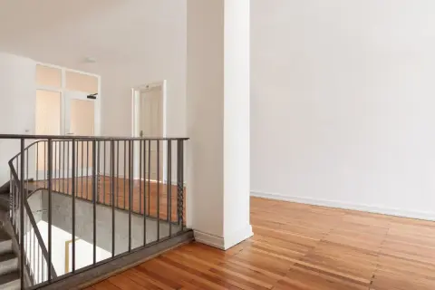 Jak pomalować wysoką klatkę schodową? Jasne wnętrze z drewnianą podłogą i metalową balustradą.