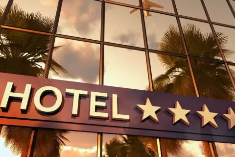 Hotel z czterema gwiazdkami, odbijający palmy i samolot w zachodzącym słońcu.