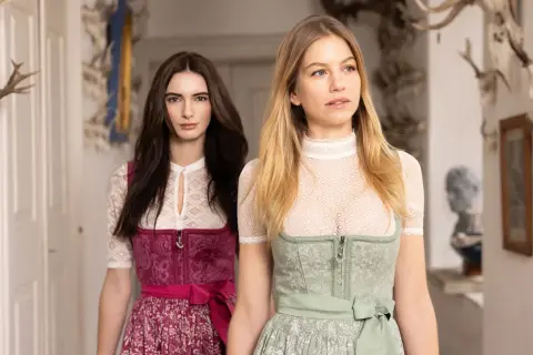 Zwei Frauen in Tracht, eine mit dunkelbraunem, die andere mit blondem Haar, präsentieren elegante dirndlschürzen lang.