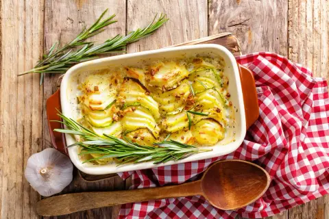 Gratin de pommes de terre et courgettes, une idée pour cuisiner la pomme de terre en 45 recettes originales. Servi avec du romarin et de l'ail.