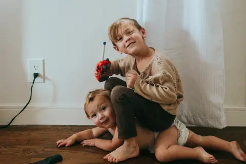 Twee broertjes spelen op de grond. De oudste zit op de rug van de jongste en houdt een speelgoedwalkietalkie vast. Dit is waarom maken broers en zussen ruzie.