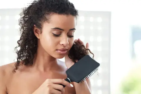 Mujer con pelo rizado y enredado, intentando desenredar con un cepillo negro.