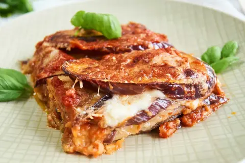 Parmigiana di Melanzane auf einem Teller mit Basilikum garniert.