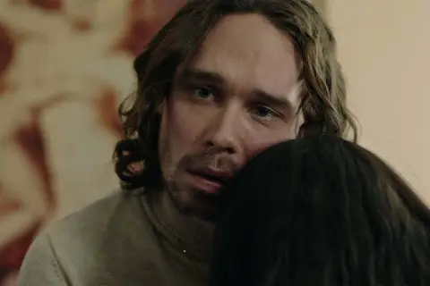 En man med långt hår och blå ögon kramar någon i tv-serien "Rollistan i Knutby".