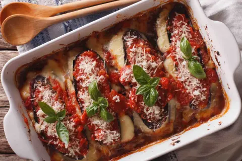 Un plat d'aubergine à la parmesane gratinée, garni de sauce tomate, fromage fondant et basilic frais.