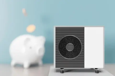 Scaldacqua a pompa di calore: svantaggi e risparmio. Un salvadanaio a forma di maialino con monete che cadono, accanto a un'unità esterna.