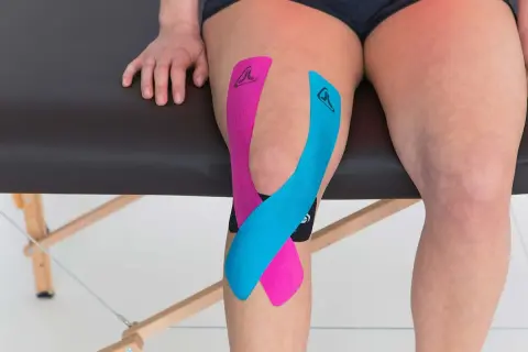 Taping genou arthrose : bandes de kinésiologie rose et bleue appliquées sur un genou pour soulager la douleur.