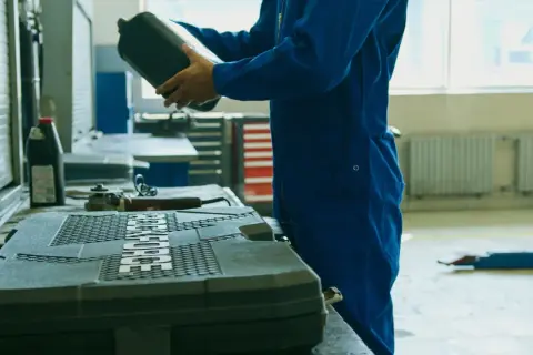 Meccanico in tuta blu prepara il cambio olio motore fuoribordo 4 tempi, tenendo una tanica di olio.