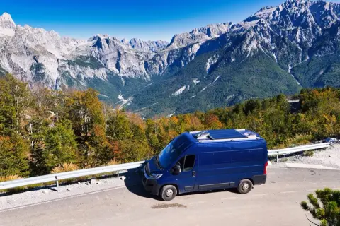 Blauer Campervan auf Bergstraße in Albanien. Perfektes Wetter im August für eine Reise durch die beeindruckende Berglandschaft.