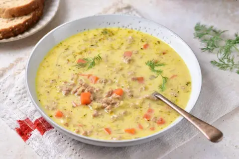 Kremowa zupa z pora z serkiem topionym i mięsem mielonym, ozdobiona koperkiem. Obok kromki chleba.