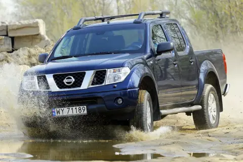 Niebieski Nissan Navara pokonuje wodną przeszkodę, rozpryskując błoto.
