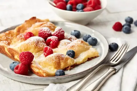 Ein goldbrauner Ofenpfannkuchen, bestäubt mit Puderzucker und garniert mit frischen Himbeeren und Blaubeeren. Perfekt für ein leckeres Ofenpfannkuchen Rezept.