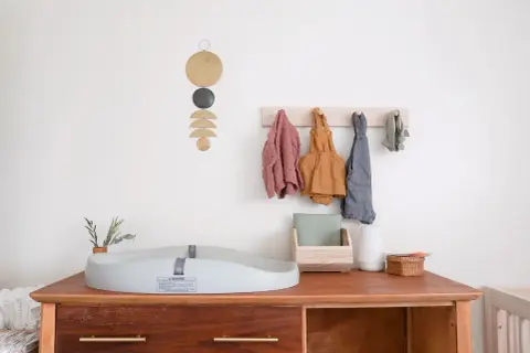 Chic corner nursery ideas: A changing pad sits on a wooden dresser with baby clothes hanging on a wall rack.
