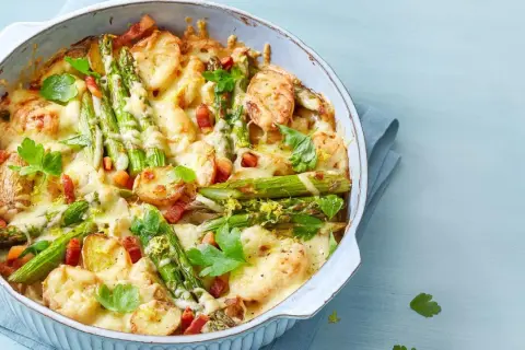 Herzhafter Spargel Auflauf mit Kartoffeln, Speck und geschmolzenem Käse, garniert mit Petersilie und Zitronenschale.